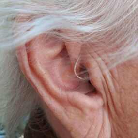 Nahaufnahme eines Ohrs mit grauen Haaren und einem modernen Hörgerät für Senioren.