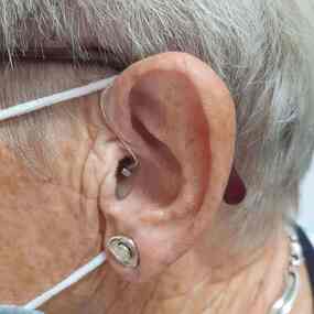 Seniorin mit Hörgerät am Ohr und Maske, Hörakustik und Hörhilfe im Alltag.