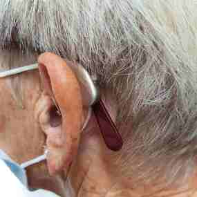 Nahaufnahme eines Ohrs mit Hörgerät bei einer älteren Person mit grauen Haaren.